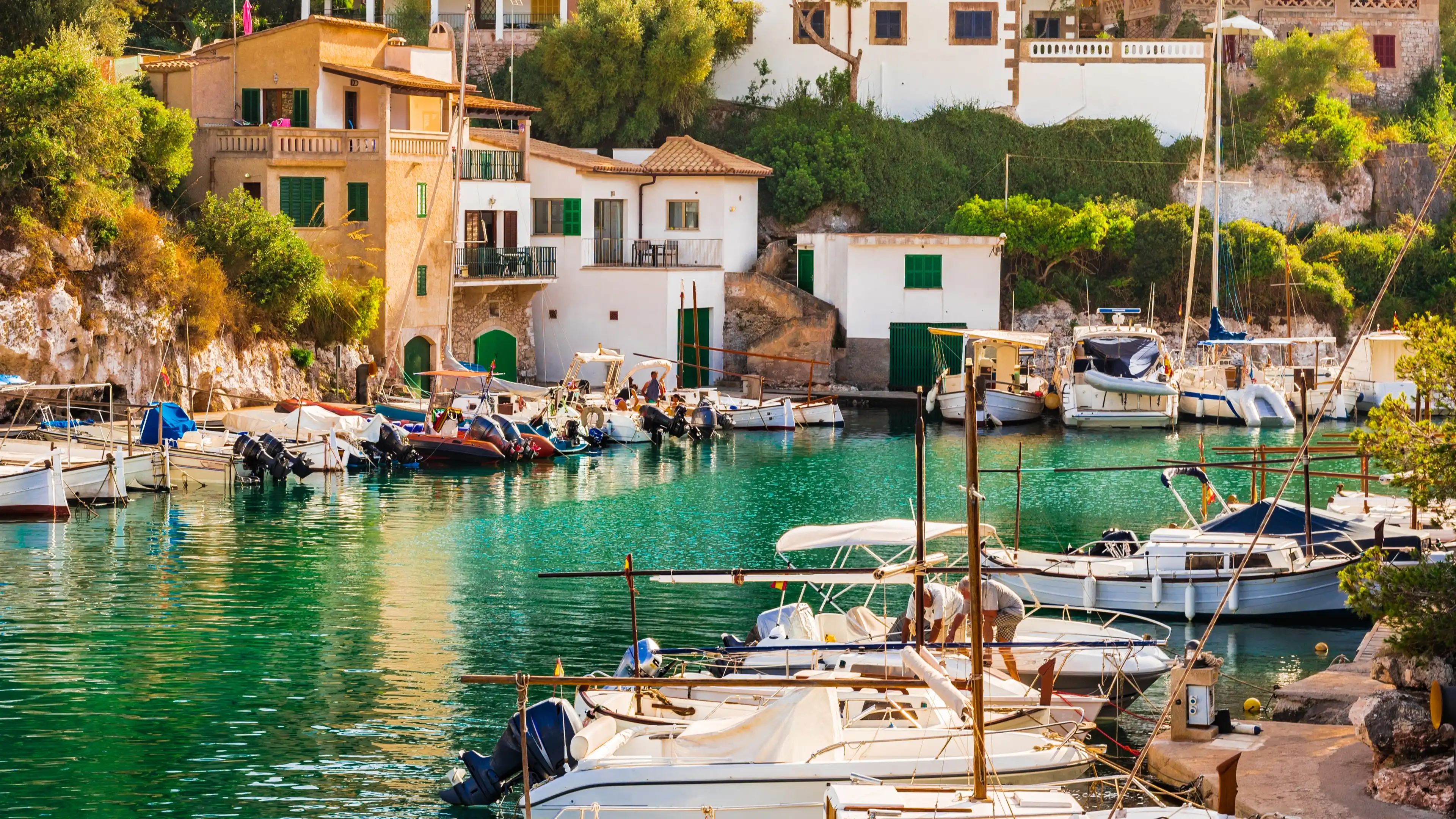 Malerischer kleiner Hafen auf Mallorca mit traditionellen Fischerbooten, türkisfarbenem Wasser und charmanten Häusern direkt am Ufer.