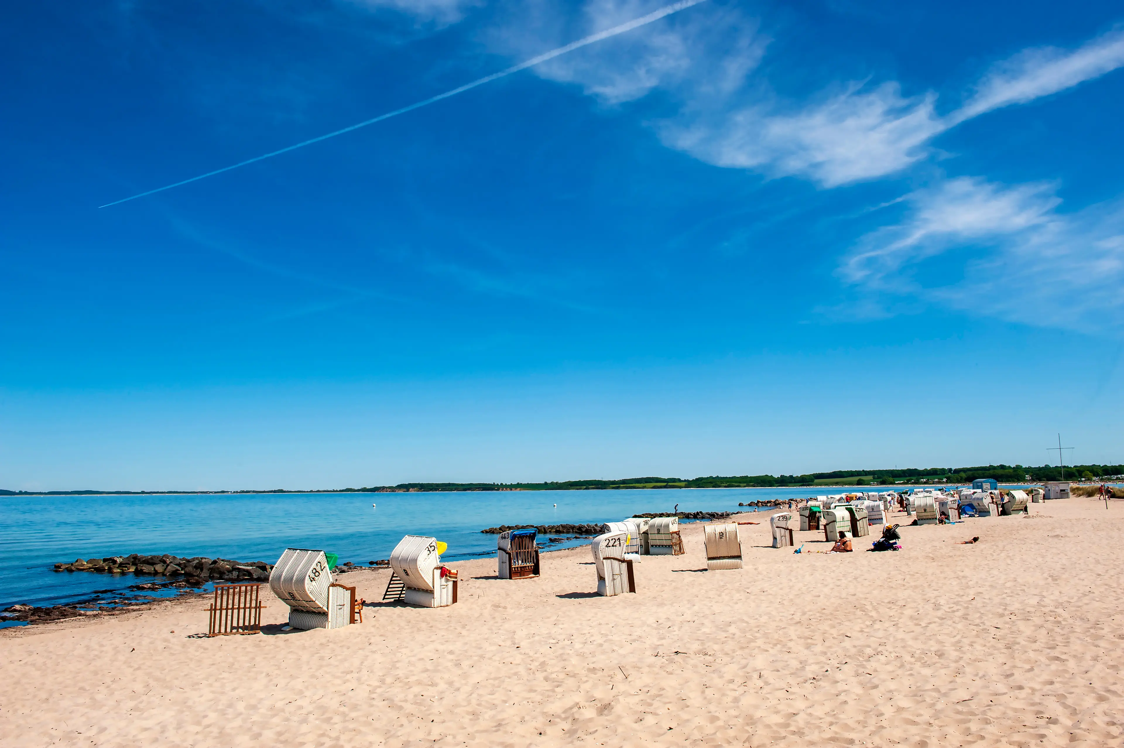 Weitläufiger Ostseestrand mit Strandkörben, feinem Sand und ruhigem Meer bei sonnigem Wetter.