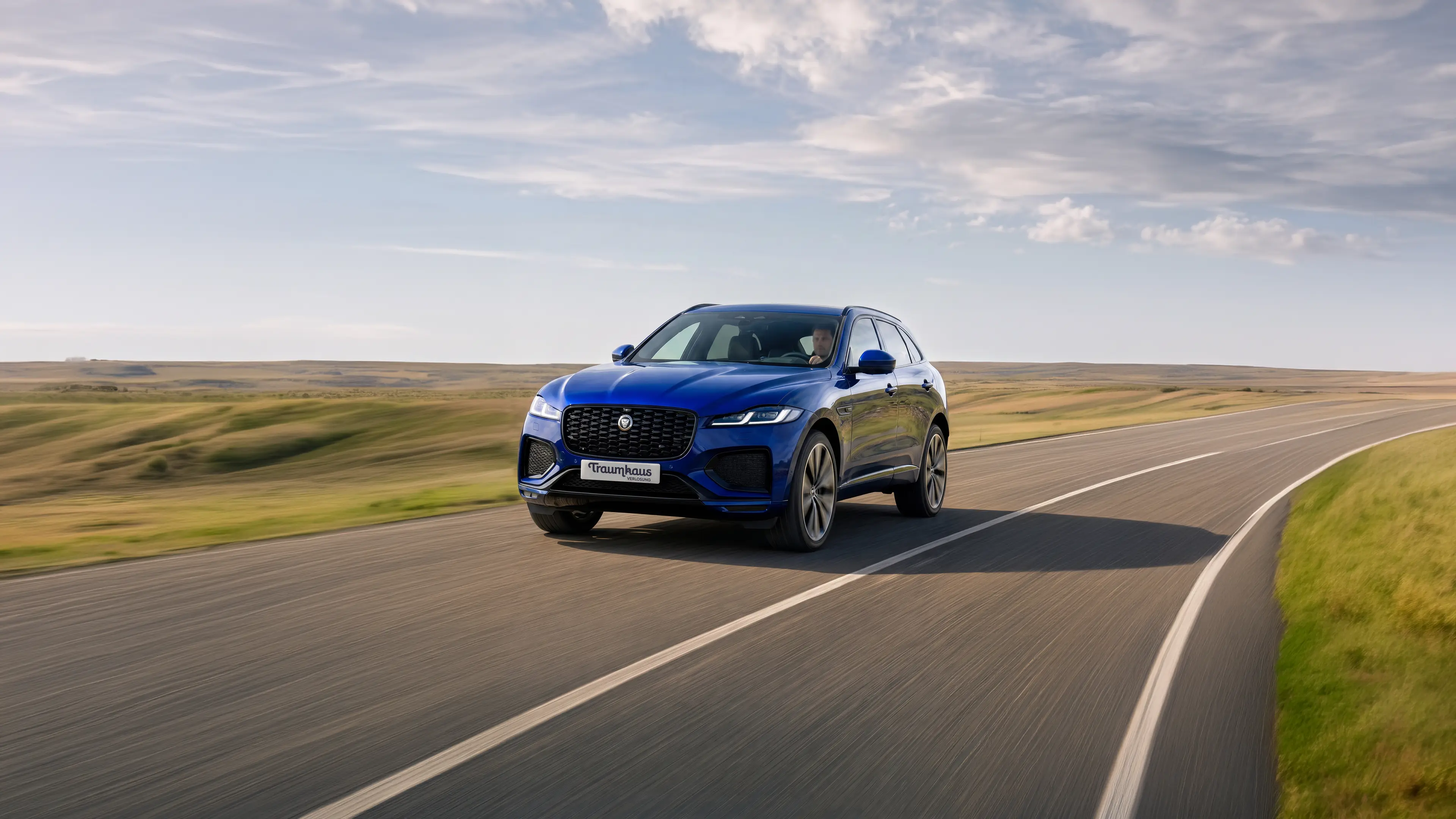 Ein blauer Jaguar F-Pace von vorne/leicht seitlich fotografiert auf einer Landstraße