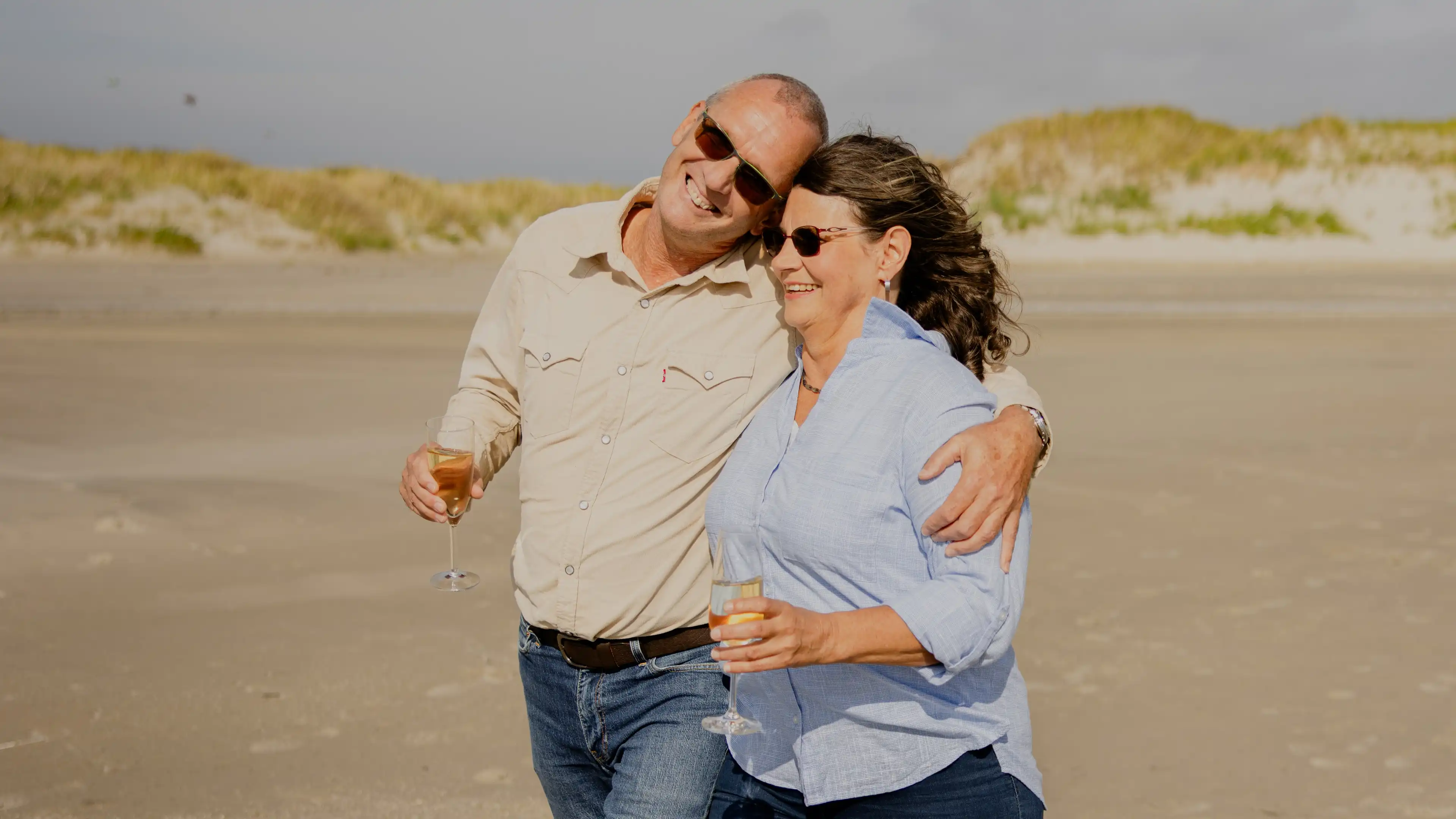 Thomas, Gewinner des Nordsee-Traumhauses und seine Frau laufen glücklich Arm im Arm am Strand von SPO entlang