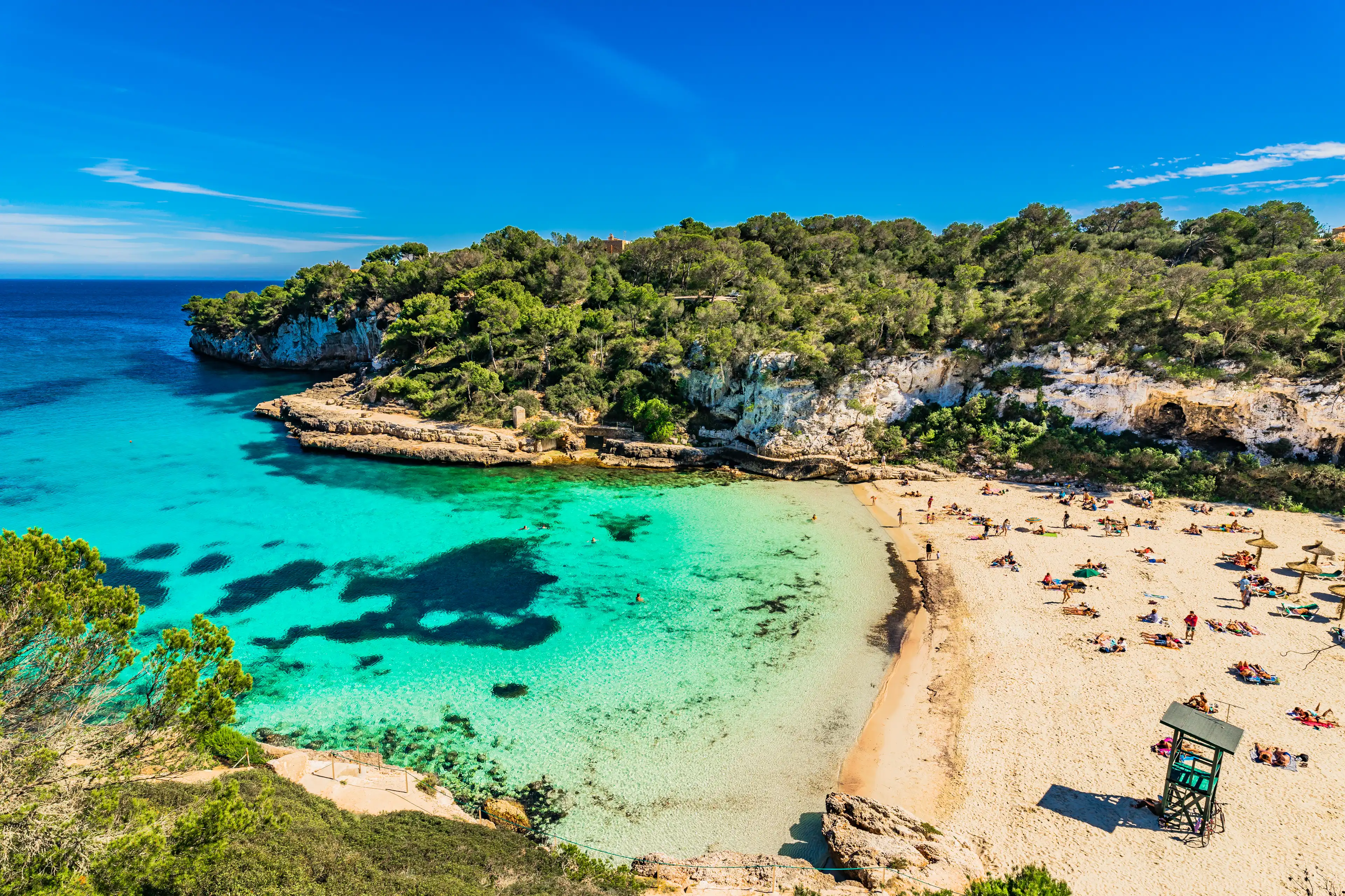 Türkisblauer Strand von Mallorca mit feinem Sand, kristallklarem Wasser und umgebenen Fels- sowie Pinienlandschaften – ein beliebtes Naturparadies der Insel.