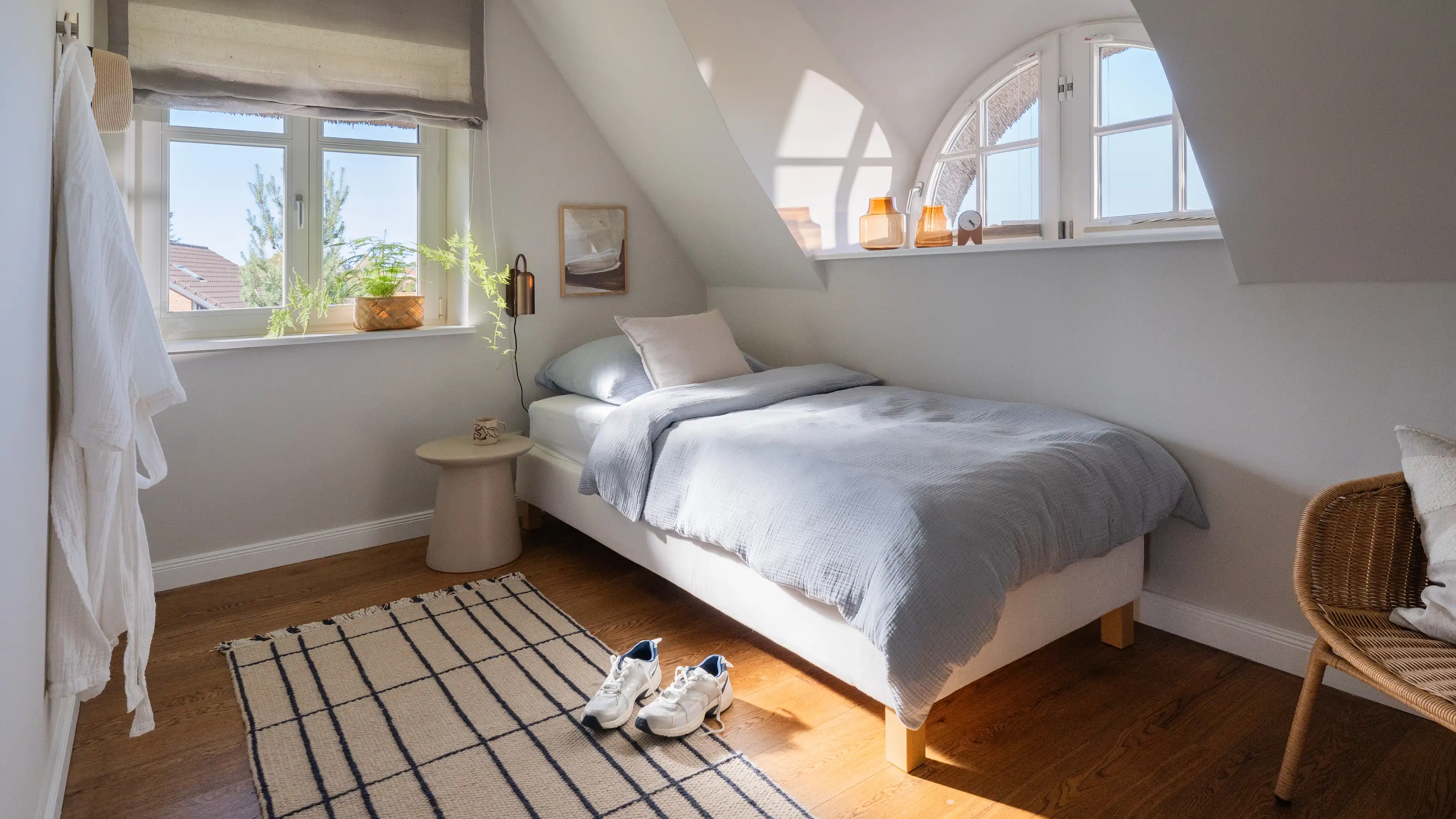 Kleineres Gästezimmer unter Dachschräge mit Bogenfenster, Einzelbett und hellgrauer Leinen-Bettwäsche.