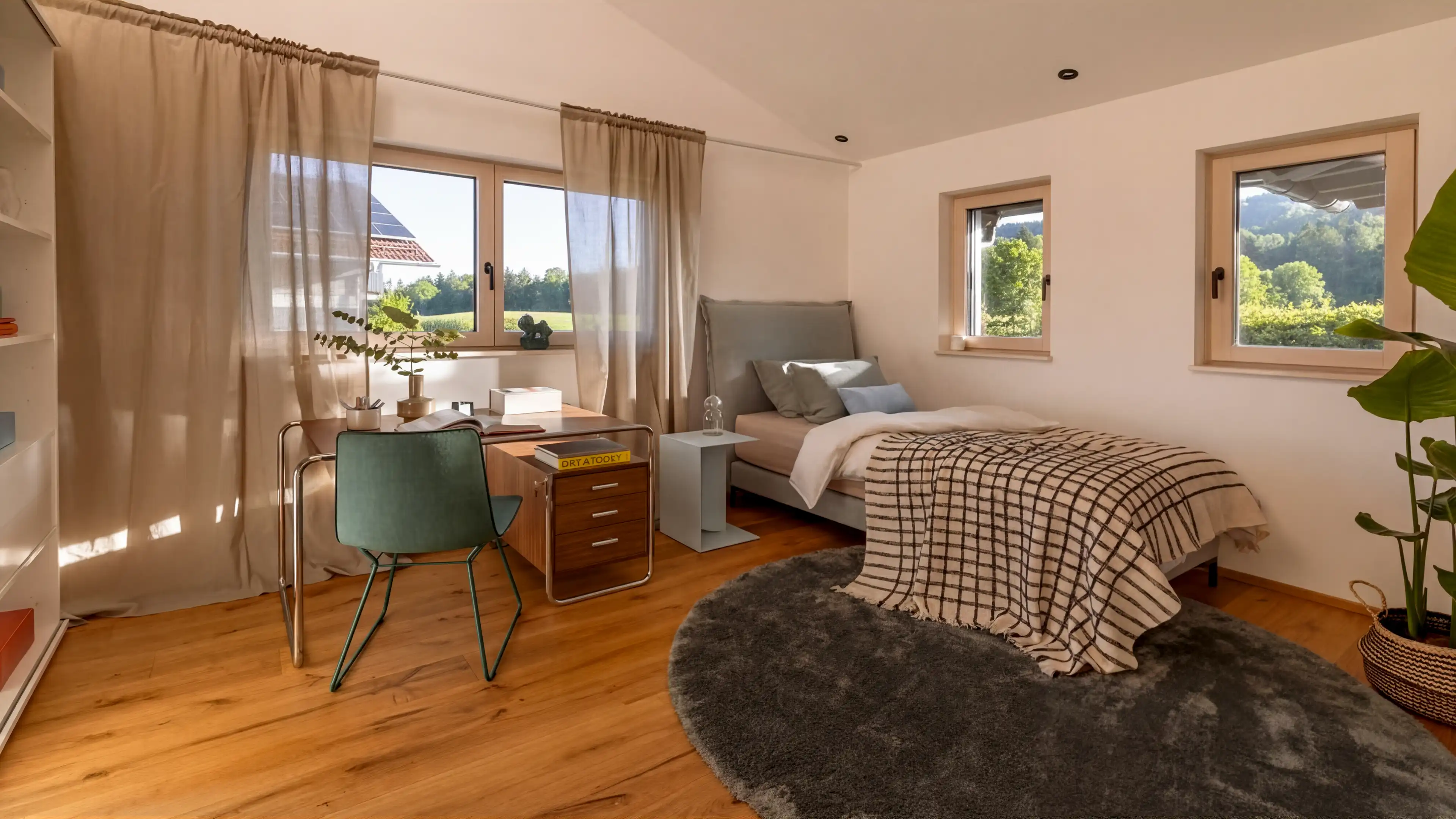 Das zweite Schlafzimmer im Traumhaus am Chiemsee mit hellgrauem Einzelbett dekoriert mit heller Bettwäsche und weiß-schwarz karierter Tagesdecke. Auf der rechten Seite neben dem Bett befindet sich ein Schreibtisch aus Holz und Glass und ein türkiser Schreibtischstuhl, welcher vor einem Fenster steht.