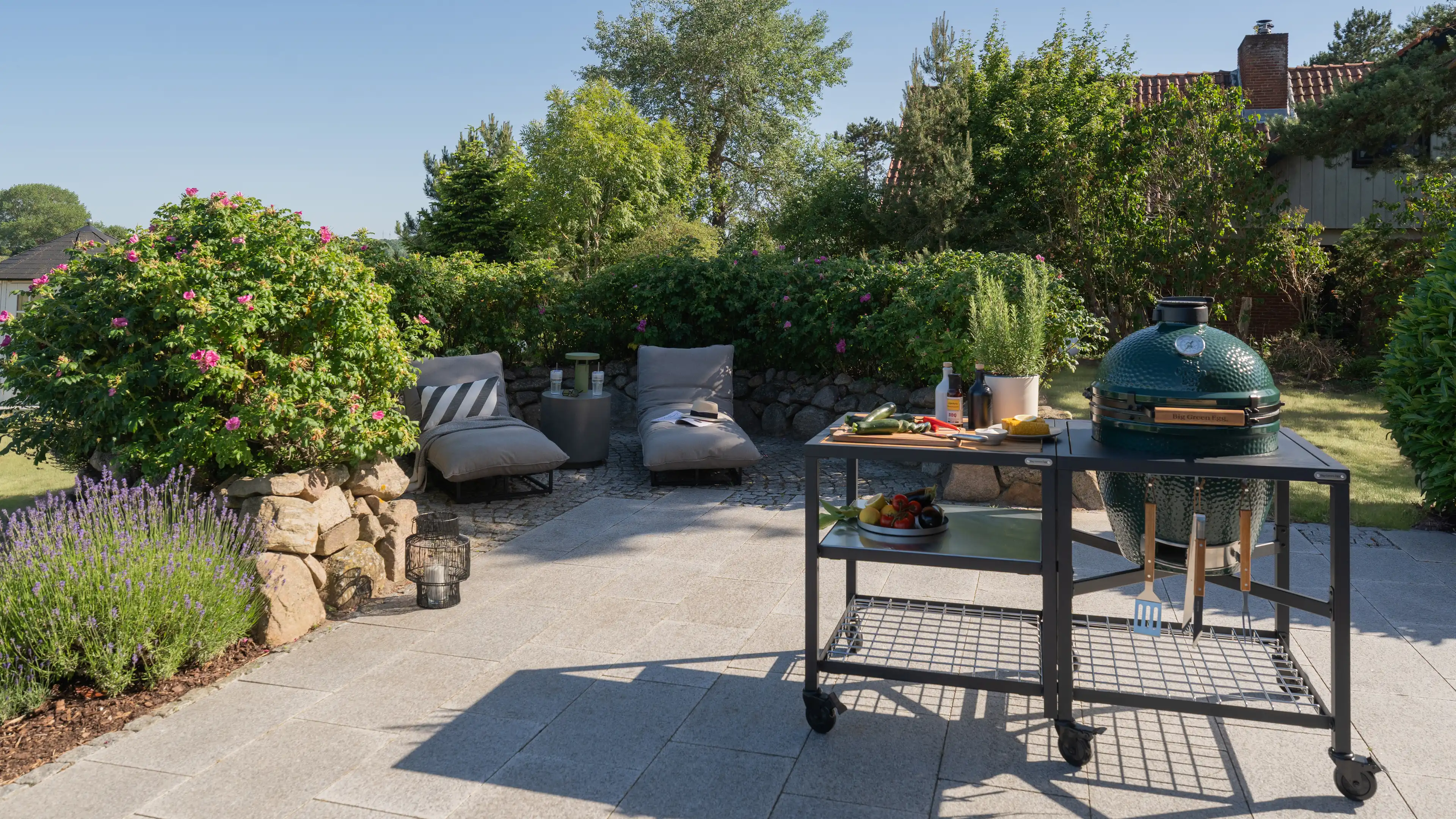 Terrasse mit zwei Loungesesseln, Rosen und Lavendel sowie einem fahrbaren Grillwagen mit Big Green Egg Keramikgrill.