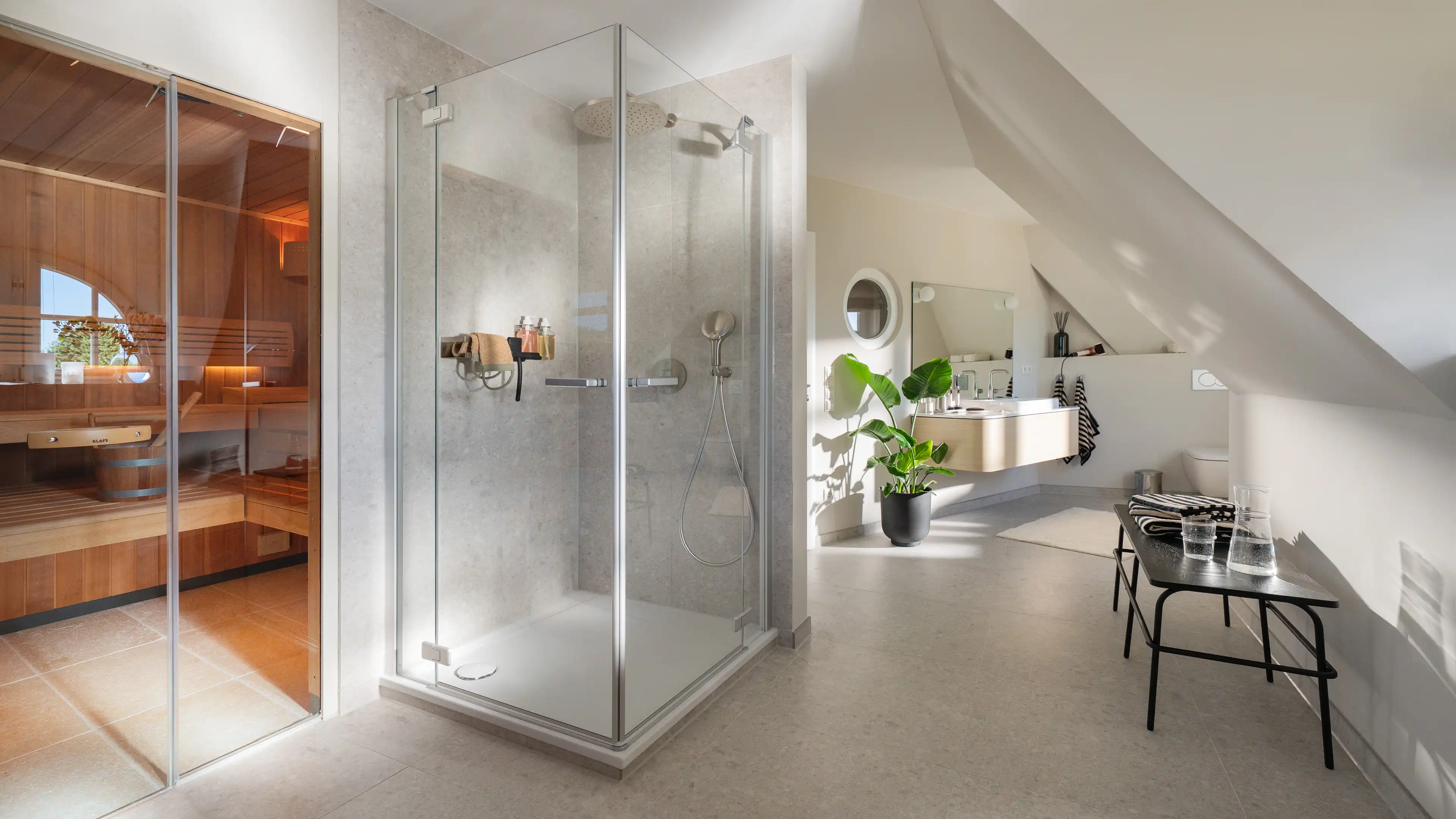 Bad mit verglaster Regendusche, Blick durch eine Glastür zur Sauna und einem Doppelwaschtisch im Hintergrund.