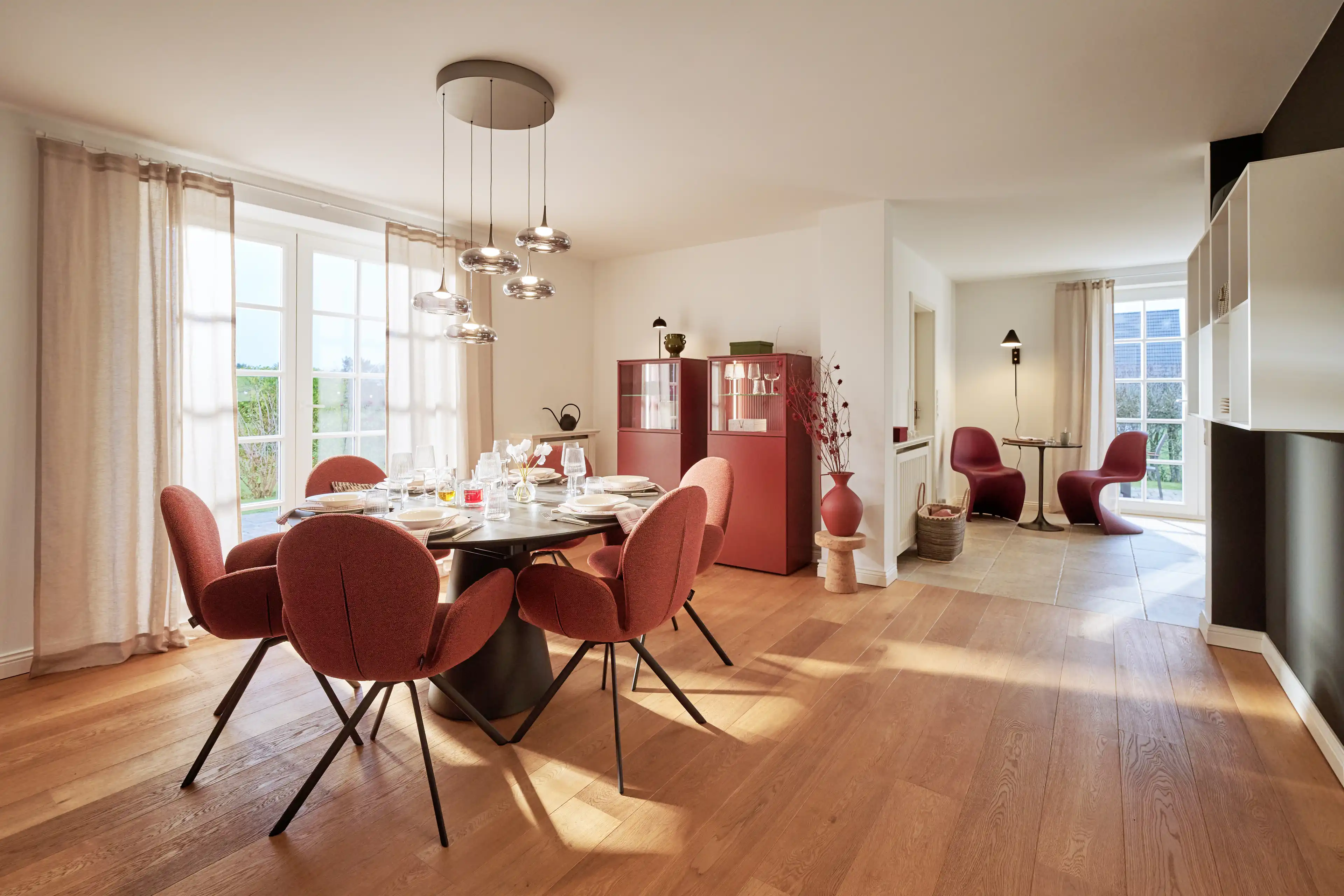 Stilvoll gedeckter Esstisch mit insgesamt 6 Stühlen mit modernen roten Designakzenten und großer Fensterfront, die für Helligkeit sorgt.