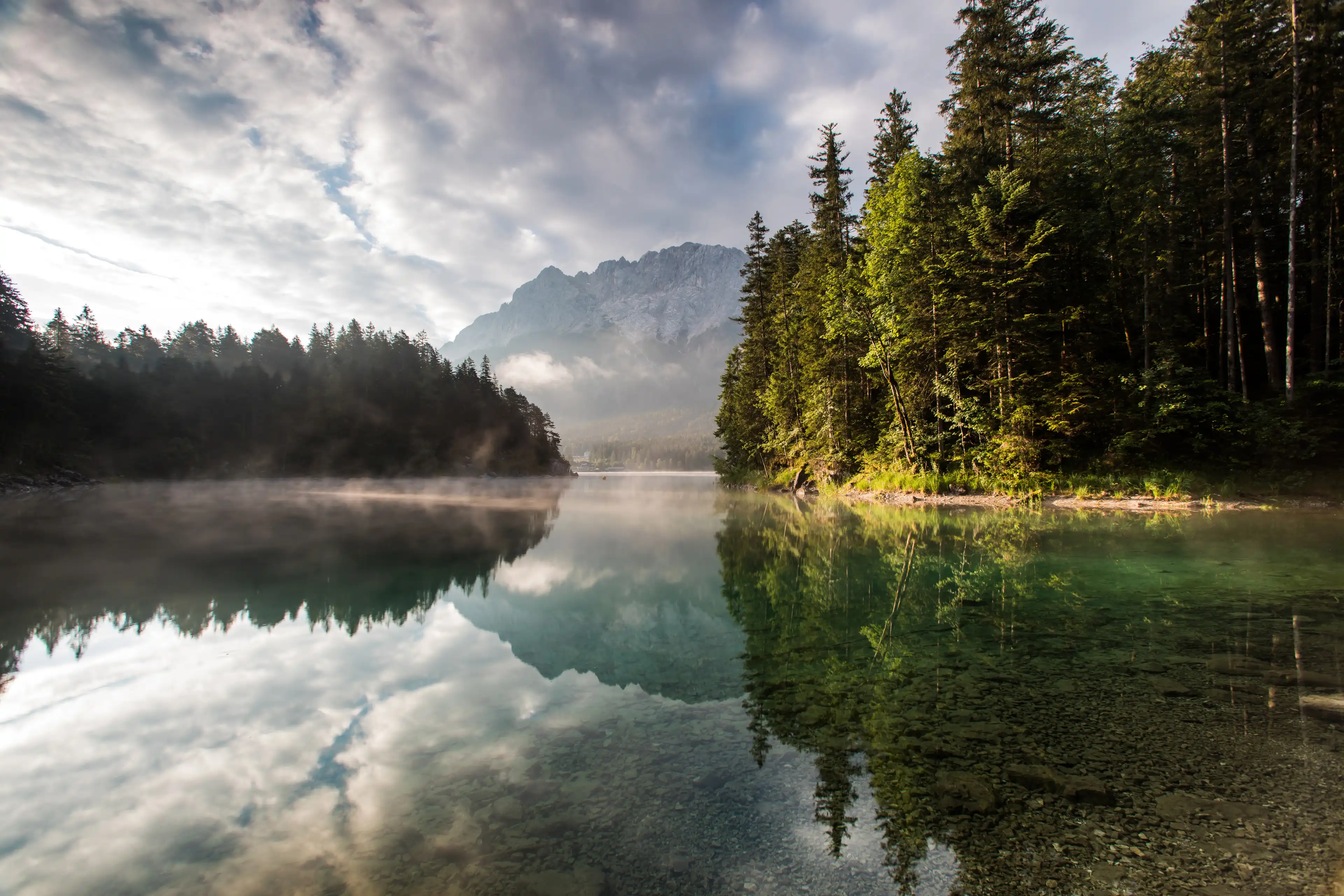 Blick auf einen glasklaren See umgeben von Wäldern und in Bergen