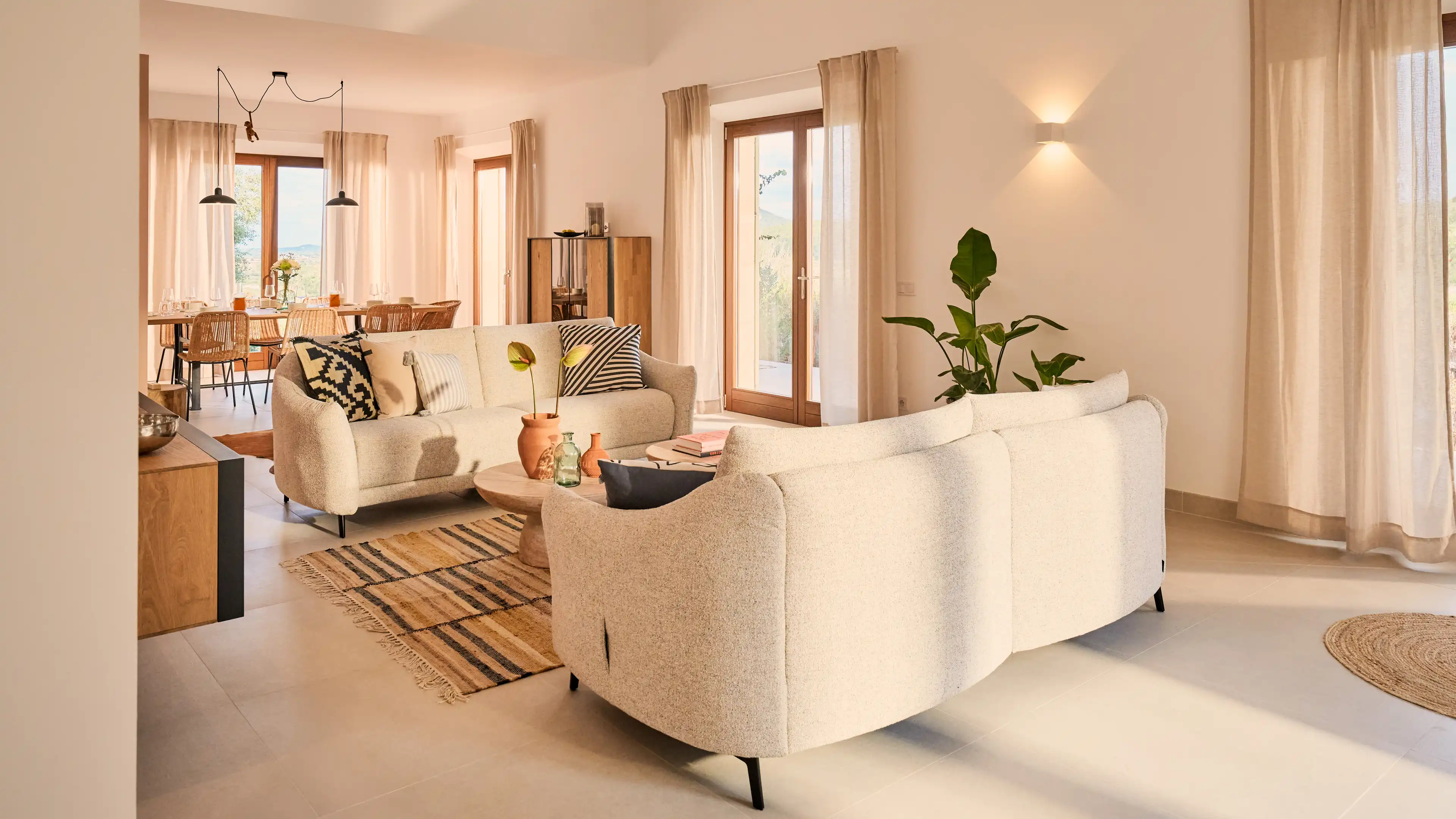 Modernes Wohnzimmer im Traumhaus auf Mallorca mit hellen Sofas, natürlichen Materialien und Blick auf den Essbereich.
