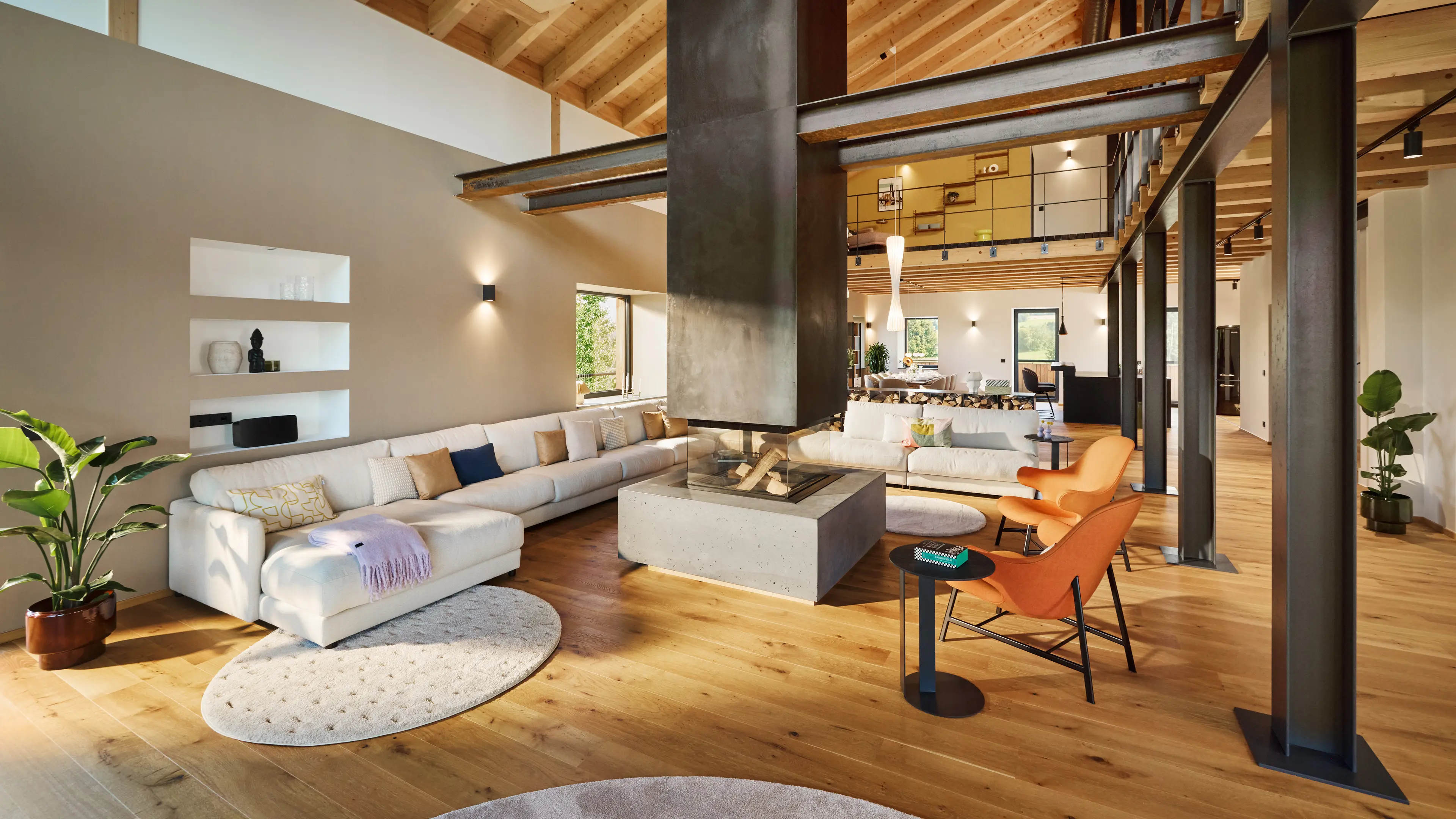 Große offene Wohnzimmer im Industrial-Stil, die creme-farbende Couch und der große Kamin bilden das Zentrum des Raumes