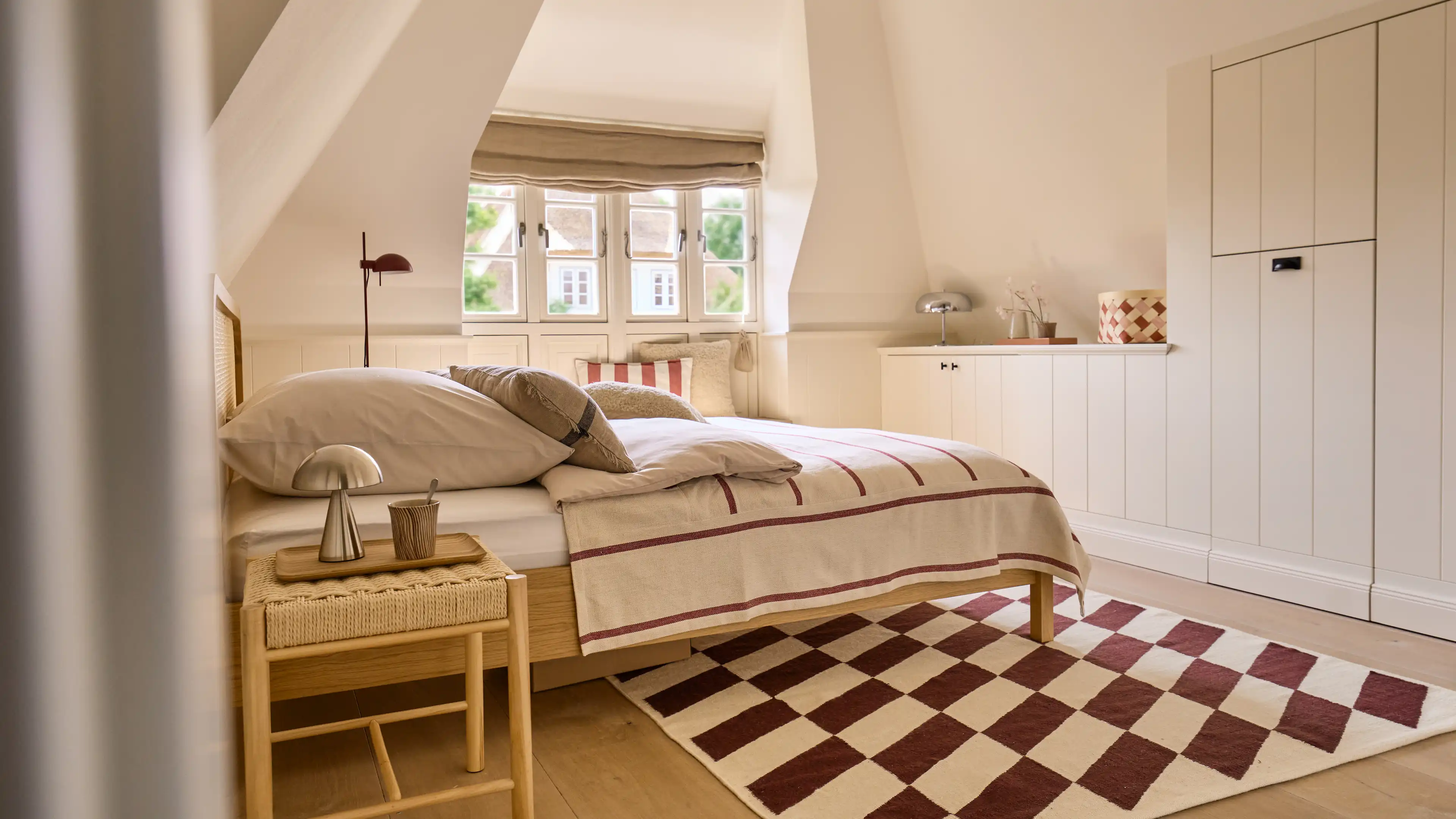Das Hauptschlafzimmer mit goßem King-Size Bett in pastell blau und gelb gehaltenden Akzenten. Neben dem Bett, ist eine kleine Sitznische direkt vor den Fenstern zu sehen.
