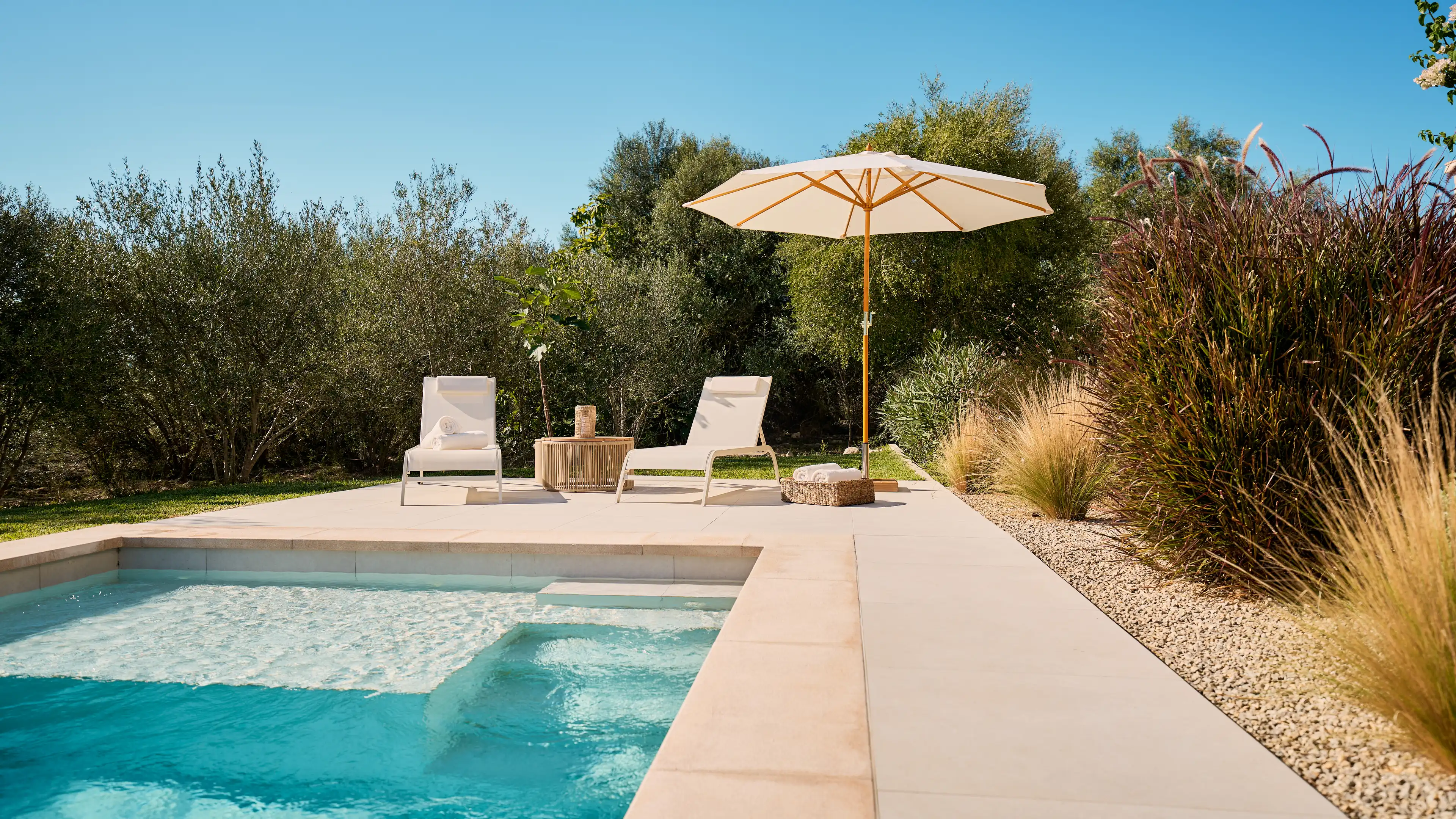 Moderner Pool im Traumhaus auf Mallorca mit türkisblauem Wasser, Sonnenliegen und Sonnenschirm – umgeben von mediterranen Pflanzen und Natur.