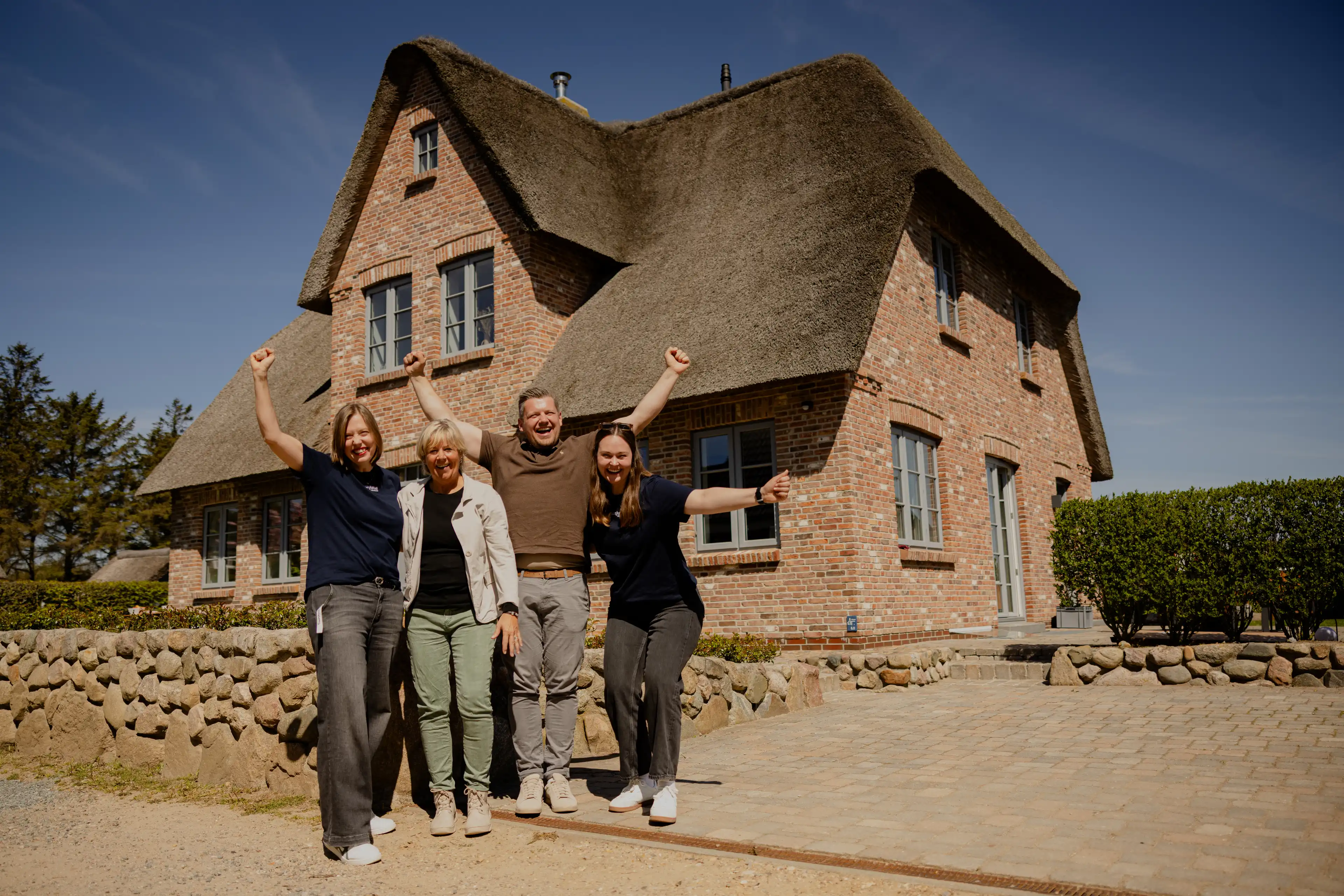 Gewinnerin Birgit mit Sohn und dem Team der Traumhausverlosung jubelnd vor dem Traumhaus auf Föhr